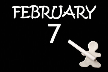 A small white plasticine man writing the date 7 February on a black board. Business concept. Education concept.