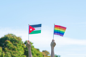hands showing LGBTQ Rainbow and Jordan flag on nature background. Support Lesbian, Gay, Bisexual, Transgender and Queer community and Pride month concept