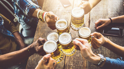 Naklejka na ściany i meble Group of people cheering beer glasses in brewery pub restaurant - Friends celebrating happy hour weekend sitting in bar table - Beverage lifestyle concept