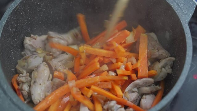 The cook mixes the zirvak for cooking pilaf in a cast-iron pot. Fried carrots, onions, spices and chicken thigh fillet