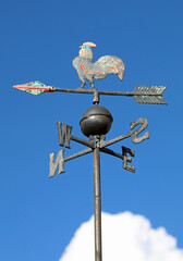vane to indicate the direction of the wind with the initials of the cardinal points and the steel cock on the top - obrazy, fototapety, plakaty