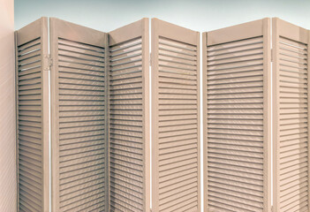 Two sets of partially open wooden bifold Venetian doors in front of a light blue room, nobody