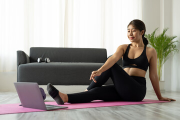 Fit sporty young asian woman online workout exercise at home. Active healthy girl enjoy sport pilates yoga fitness training on laptop computer stretching on yoga mat watching video class