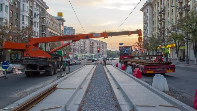 Orange construction telescopic mobile crane unloading tram rails from truck timelapse.