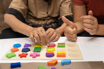 Naklejka premium Caregiver and senior woman playing wooden shape puzzles game for dementia prevention