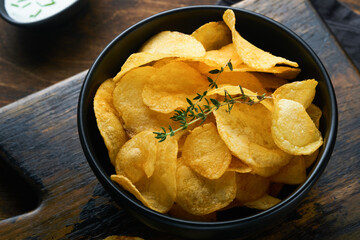 Potato chips. Fast food. Crispy potato chips ceramic black bowl with sour cream sauce and onions in wooden stand on old kitchen table wooden background. American tradition. Hot BBQ. Top view.