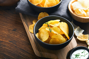 Potato corrugatedchips. Fast food. Crispy potato chips ceramic black bowl with sour cream sauce and onions in wooden stand on old kitchen table wooden background. American tradition. Hot BBQ. Top view