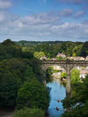 Fototapeta na wymiar Knaresborough’s viaduct and the River Nidd in bright sunshine and under a blue sky strewn with fluffy cotton-wool clouds.