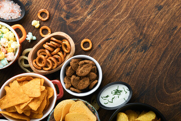 Fototapeta na wymiar Unhealthy food or snacks. All classic potato snacks with peanuts, popcorn and onion rings and salted pretzels in bowl plates on old wooden background. Unhealthy food for figure, heart, skin, teeth.