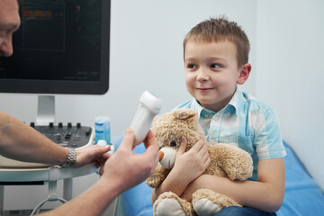 Shying boy listening attentively to the doctor sitting with him in the office