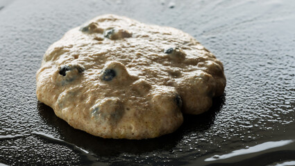 Blueberry pancake frying on a cast iron griddle pan, ready for flipping.