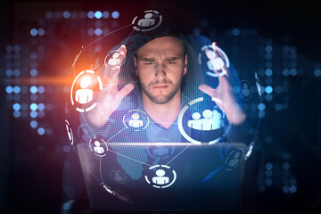 Handsome businessman in hoodie at workplace working with laptop to hire new employees for international business consulting. HR, social media hologram icons over office background