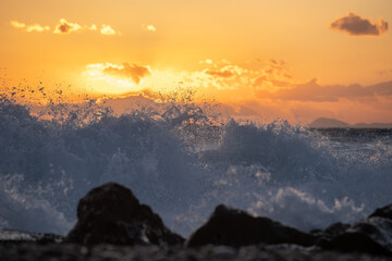 Sea ​​wave at sunnset in gold hour hitting a rock on the beach.