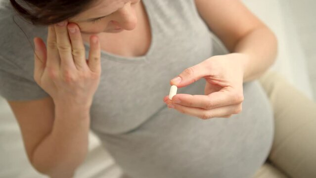 Close-up view of pill in hand. Pregnant woman strokes the belly and head. Taking vitamins during pregnancy. Health care and medication during pregnancy and childbearing. Headache and treatment