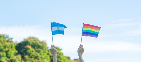 hands showing LGBTQ Rainbow and Argentina flag on nature background. Support Lesbian, Gay,...