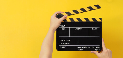 Top view. The hands are holding a black with yellow clapper board on white background.