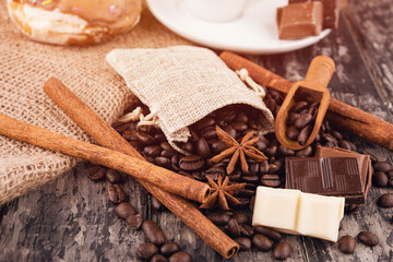 cup of coffee with chocolate, cinnamon sticks, and coffee beans on wooden background	