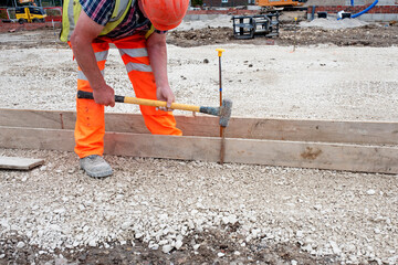 Groundworker making shutter for concrete to form a base for kerb using scaffold boards and steel road pins during new road construction