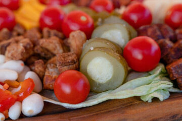 cherry tomatoes, sweet peppers,  pickled cucumbers, pickled garlic, olives,  sausage, different cheese, bacon on wooden plate. Snack food