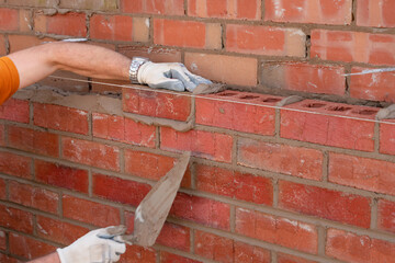 Bricklayer laying bricks on mortar on new residential house construction. Another brick in the wall