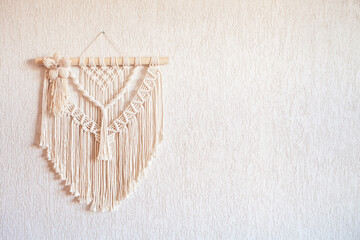 Handmade macrame wall decoration with wooden stick hanging on a white wall. Macrame braiding and cotton threads. Female hobby. ECO friendly modern knitting natural decoration in interior. Copy space