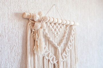 Handmade macrame wall decoration with wooden stick hanging on a white wall. Macrame braiding and cotton threads. Female hobby. ECO friendly modern knitting natural decoration in interior