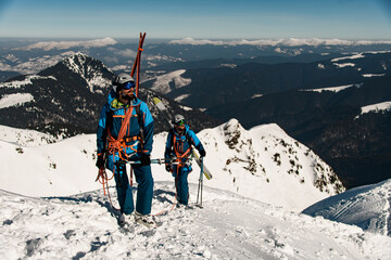 skiers in bright ski suits with ski equipment on snowy ridge.