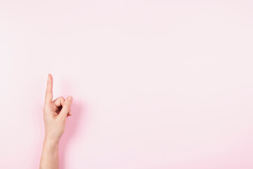 Woman hand pointing up with index finger to something virtual and invisible, copy space on pastel pink background. Hand gesture, number one