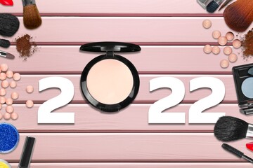 Beauty cosmetic products concept. Top view of 2022 white number with powder,  eyeshadow, brush on pink background.