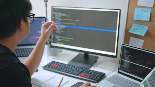 Young Asian man, developer programmer, software engineer, IT support, wearing glasses working on computer to check coding in bugging system. Back view