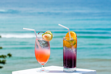 Two tropical fresh iced mocktails on the bar table with sea beach on background. Cocktails on luxury tropical vacation. Thailand Asia summer travel