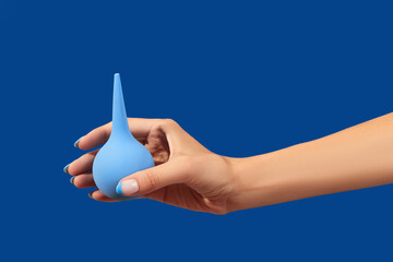Wellgroomed womans hand holding enema on blue background