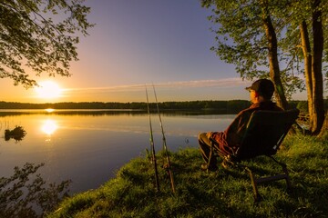 Angler sitting on fishing chair during sunrise - 500760349
