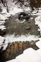 view on off-road vehicle driving through a mountain river at winter