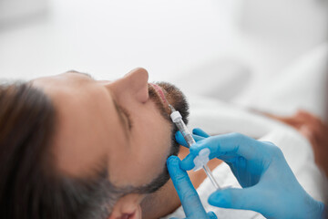 Handsome man undergoes lip augmentation with professional beautician doing filler injection in...