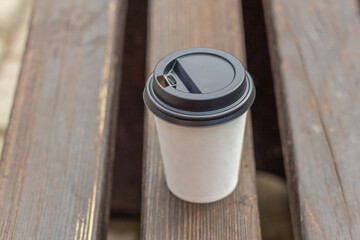 A paper cup of coffee is on a park bench.