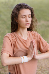 Fototapeta premium a European woman with curly hair meditates in a park. yoga and meditation for mental and physical health. a woman sits in the lotus position and namaste with her eyes closed and engages in breathing