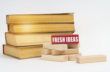 On a white surface, a stack of books and wooden blocks, on a red block there is an inscription - Fresh Ideas