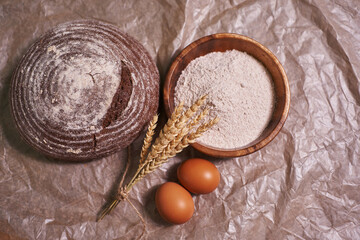 view from above. whole grain flour, eggs and freshly baked round rye bread. homemade bread with a sprig of tied ears. food background