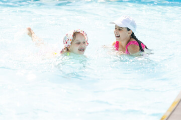 two girls splash in an outdoors swimming pool in summer. Happy children, sister playing, enjoying sunny weather in public pool