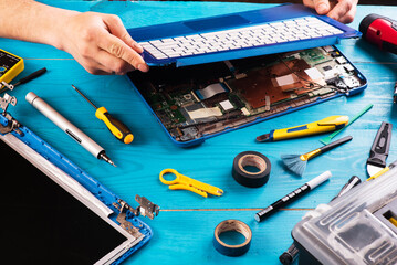 Wizard repairs laptop with tools and hands on the blue wooding table. top view