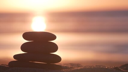 Stack of pebble stones, sandy ocean beach, sunset sky. Rock balancing in sun light, sea water waves. Stones staking in pyramid pile. Zen meditation and harmony in balance. Seamless looped cinemagraph.