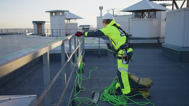 Industrial climber man in a white hard hat and work overalls pulls out a rope on the roof at the end of the working day
