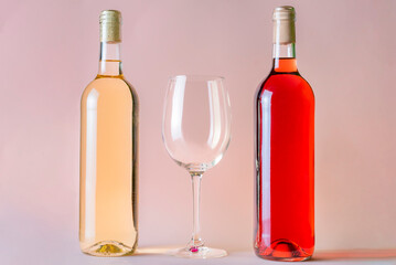 Two bottles of wine, one rosé and the other white, with an empty glass between the two, on a salmon-colored background.