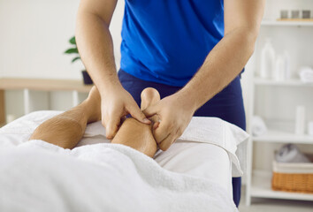 Obraz na płótnie Canvas Professional physiotherapist or masseur therapist massages calf muscle of male patient. Cropped image of man receiving leg acupressure therapy lying on massage table in wellness center.