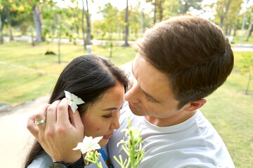 Close up view of a man putting a white flower in his wife's hair in a park