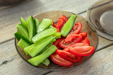 Sliced cucumbers and tomatoes on a brown glass a plate on a wooden table.