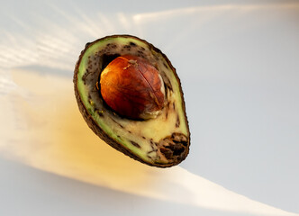 Ugly rotten avocado cut in half. Spoiled food in sunshine. High quality photo