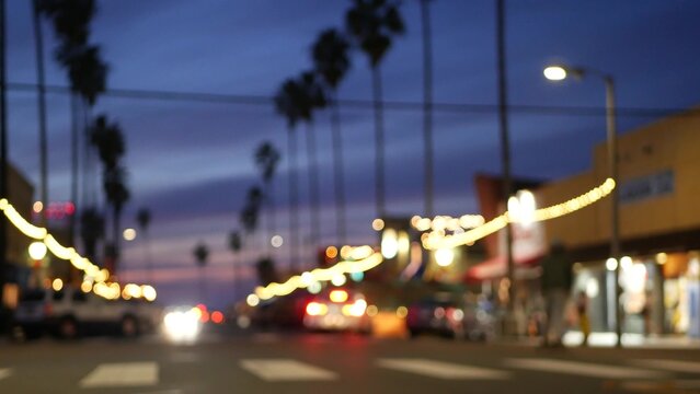 Defocused palm trees in Ocean Beach, lights in twilight, California coast, San Diego, USA. Row of palmtrees and cars on evening road in dusk. Illuminated garlands glowing on waterfront city street.
