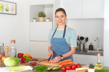 Young vegetarian woman cooking at kitchen, cutting carrot